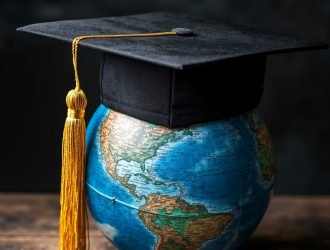 A black graduation cap with a yellow tassel on top of a globe